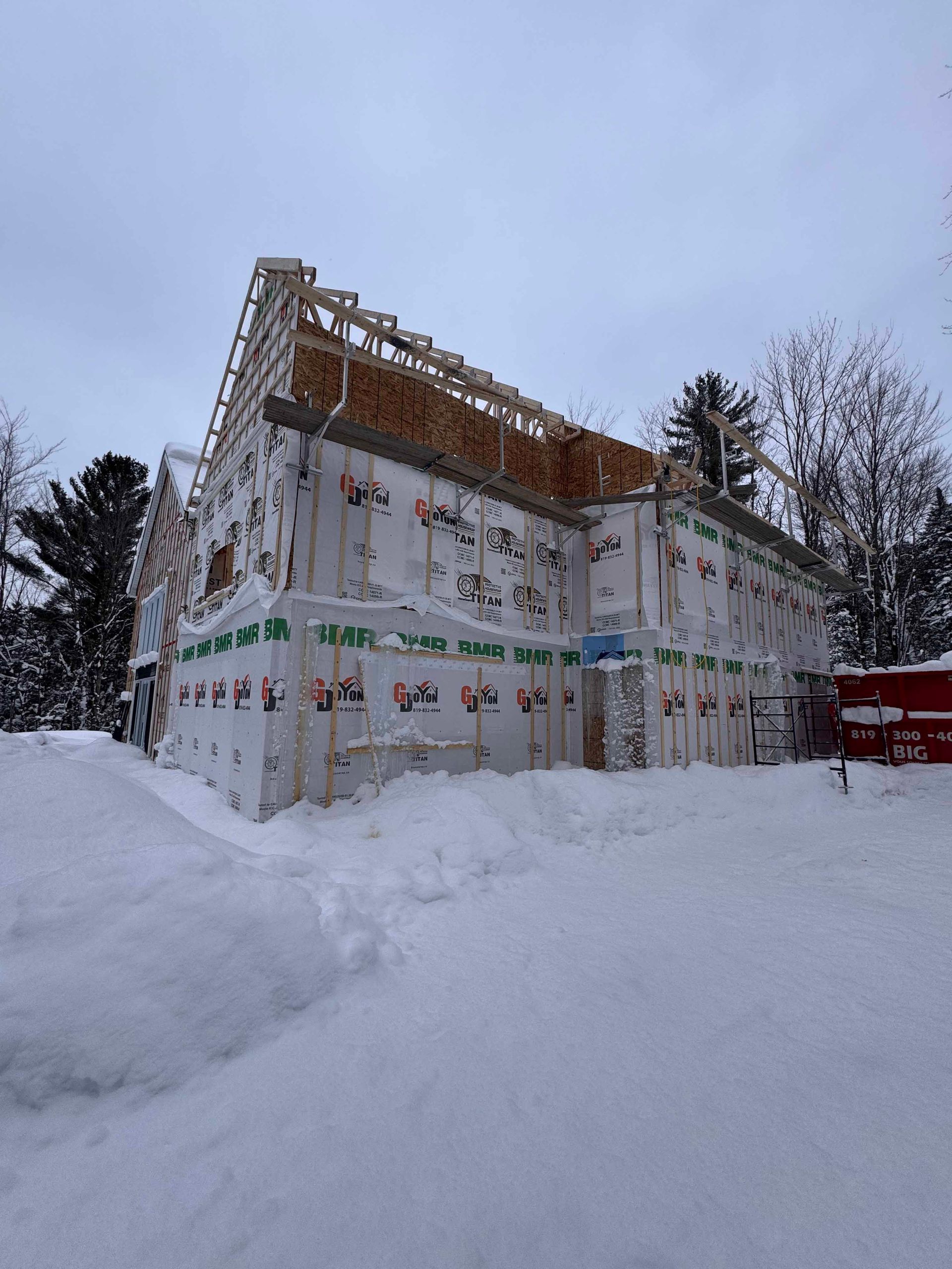 Construction d'une maison à deux étages, enveloppée d'une barrière blanche contre les intempéries, dans un environnement enneigé.