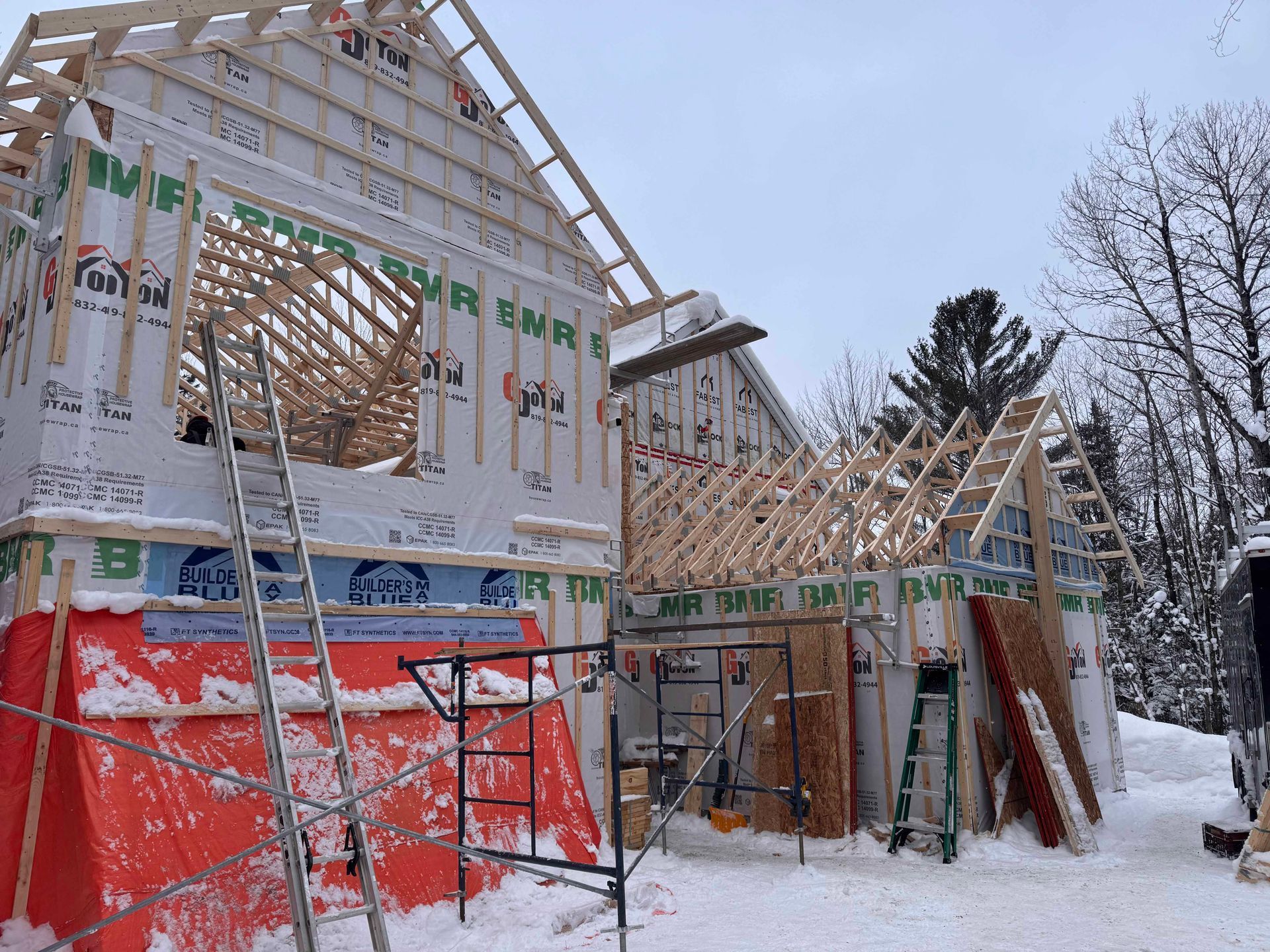 Construction d'une maison en hiver. Charpente en bois, revêtement bleu, neige au sol.