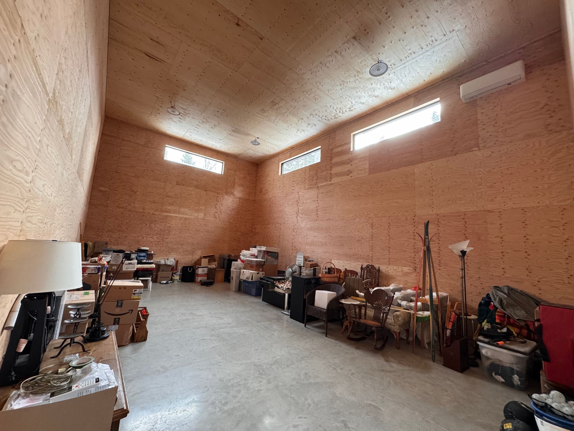 Espace de stockage rempli de cartons, de meubles et d'objets divers. Murs couleur pêche, sol en béton et lumière naturelle.