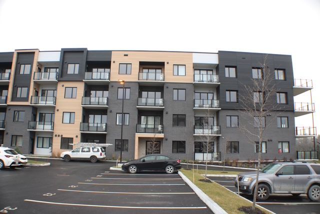 Immeuble d'appartements à plusieurs étages avec parking. Façade ornée de blocs noirs, beiges et blancs.