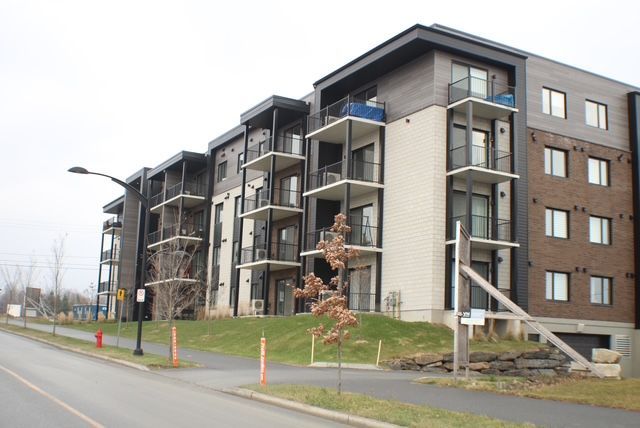 Immeuble d'appartements moderne à plusieurs étages, balcons et revêtement en brique et bois.