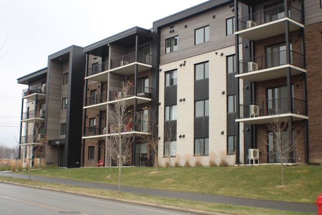 Immeuble d'appartements moderne avec balcons et finitions extérieures variées sur un terrain gazonné.