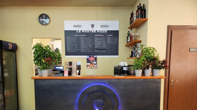 Bancone con menù, macchina del caffè, piante e scaffali con bottiglie.