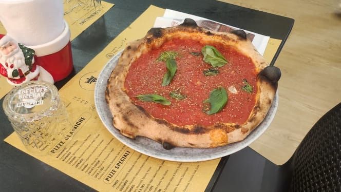 Pizza con salsa rossa e basilico su un piatto, su un tavolo con i menu e una statuina di Babbo Natale.