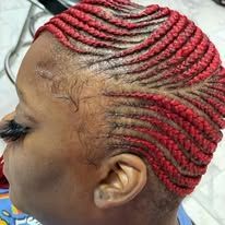 Close-up of a person's head with red cornrow braids.