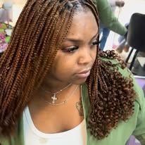 Woman with long, auburn braided hair, wearing a white top and green jacket, looking down.