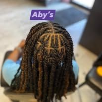 Person with dark braided hair styled in a twist. Overhead view, indoors. Blue shirt, logo: Aby's.