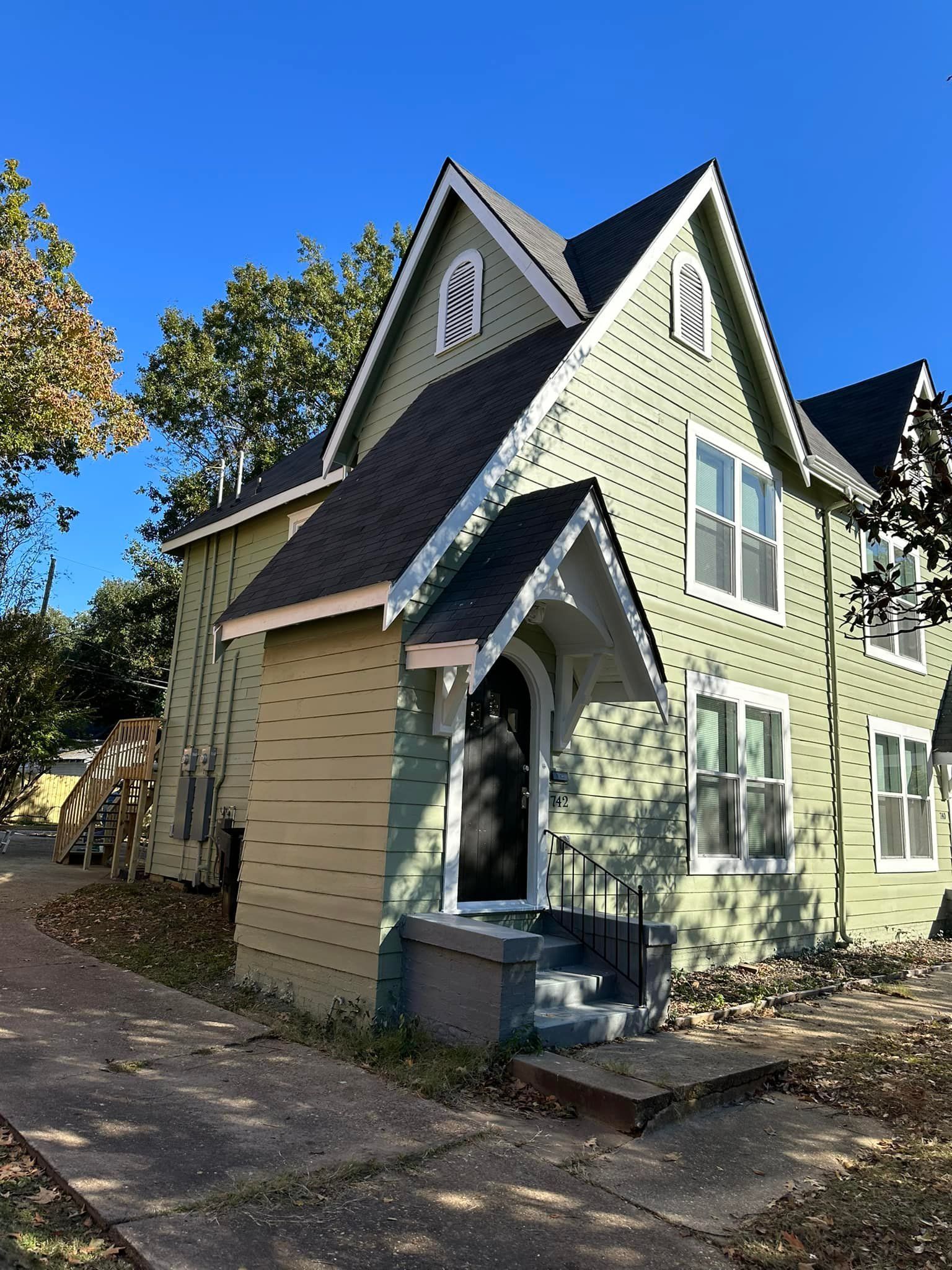 A green house with a black roof and a porch