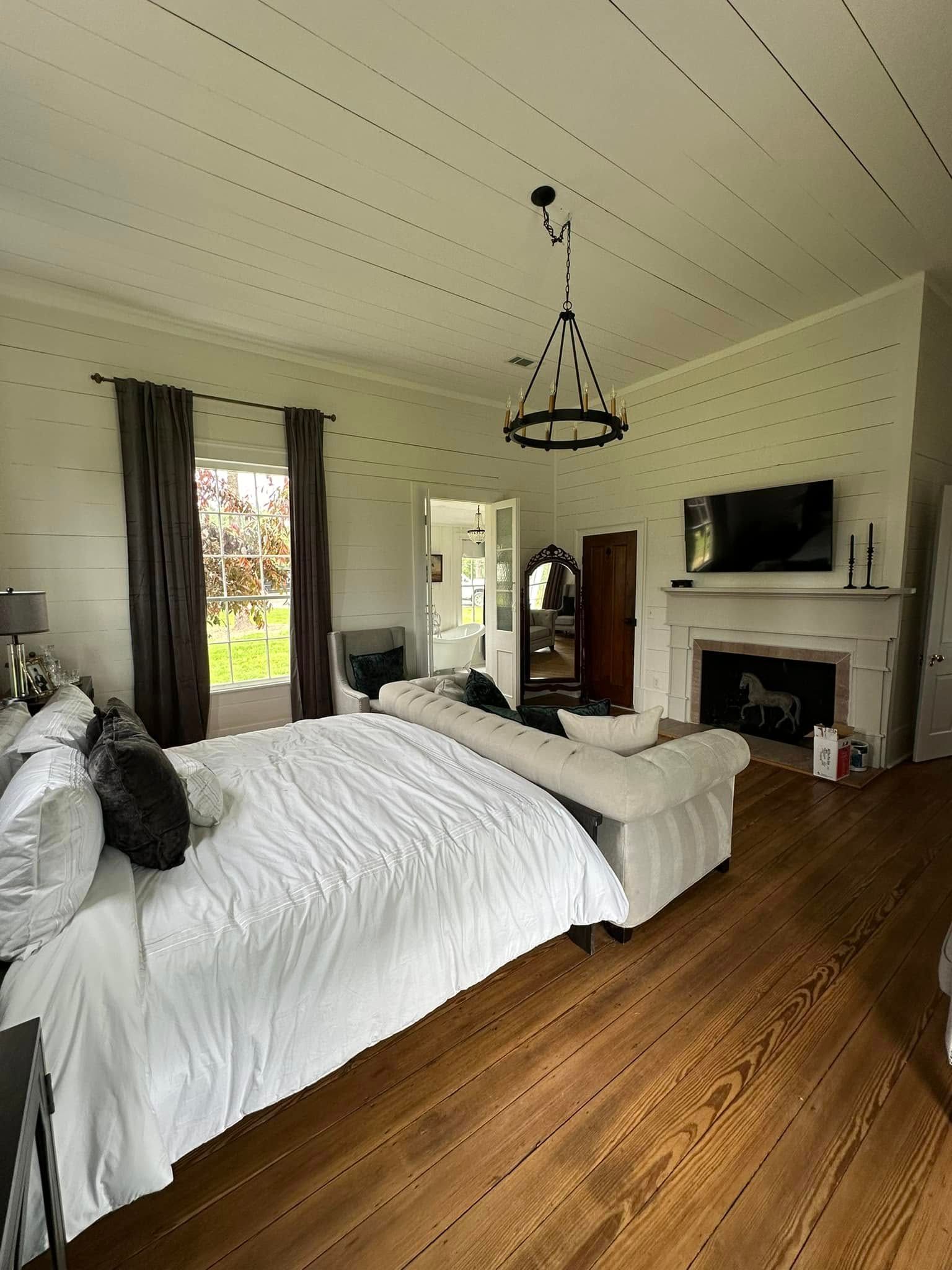A bedroom with a large bed , couch , fireplace and television.