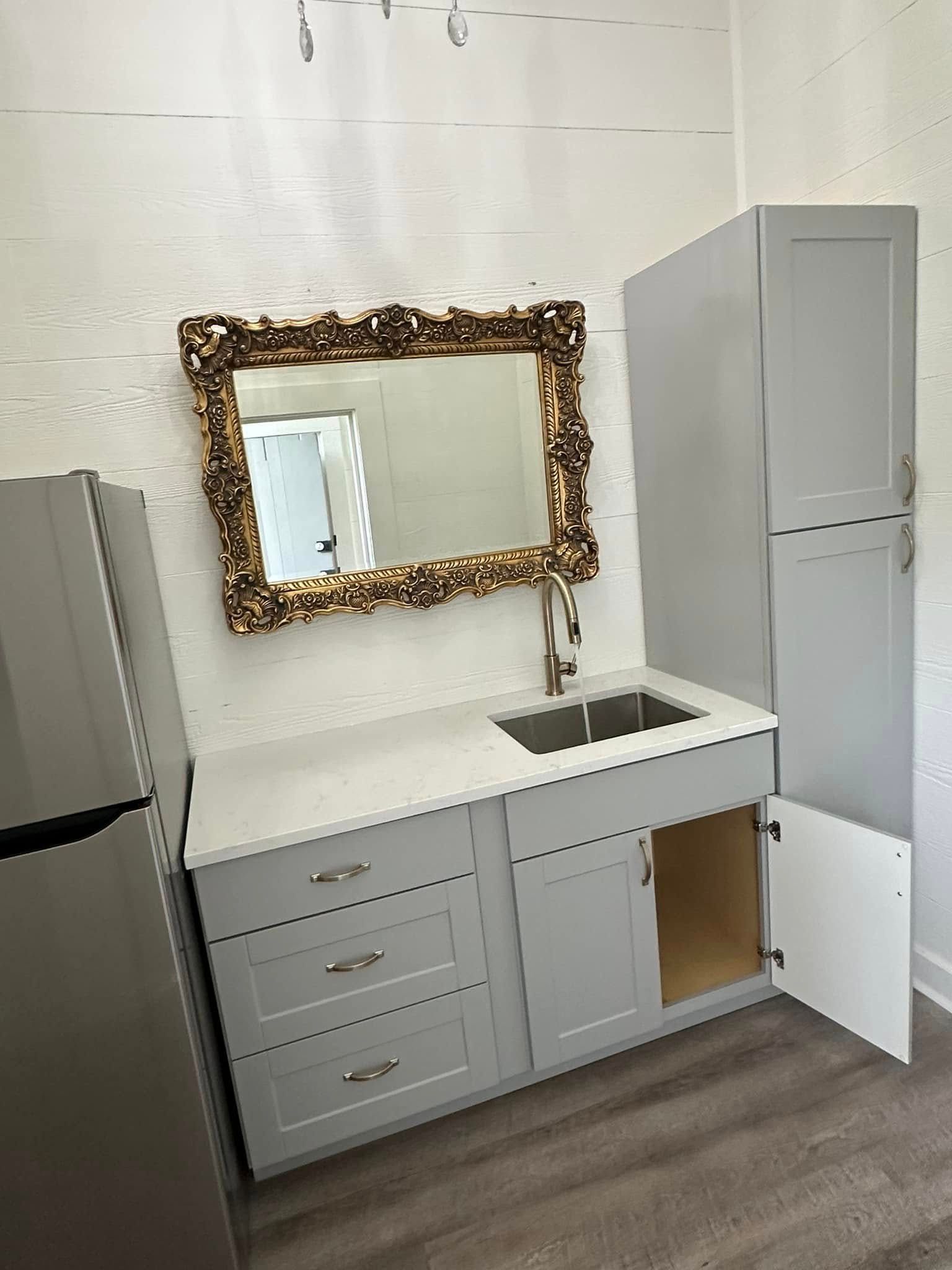 A kitchen with a sink , refrigerator , cabinets and a mirror.