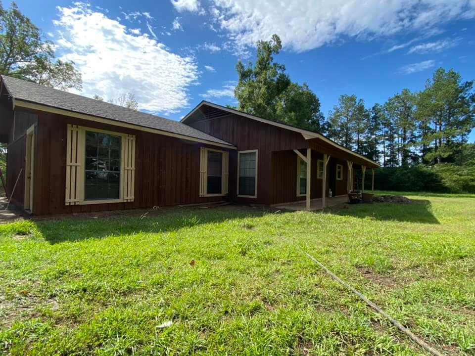 A brown house is sitting in the middle of a lush green field.