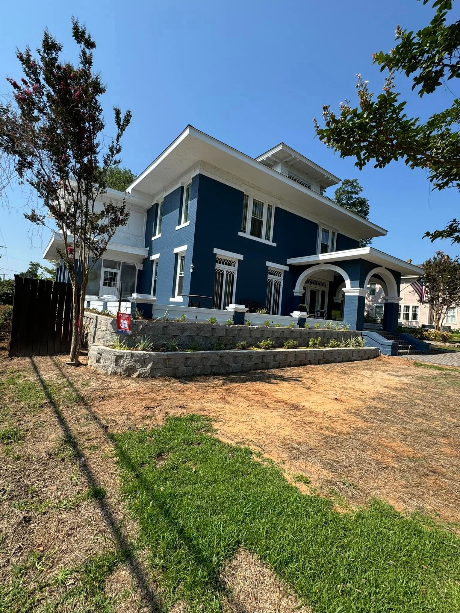 A large blue and white house is sitting on top of a lush green hillside.
