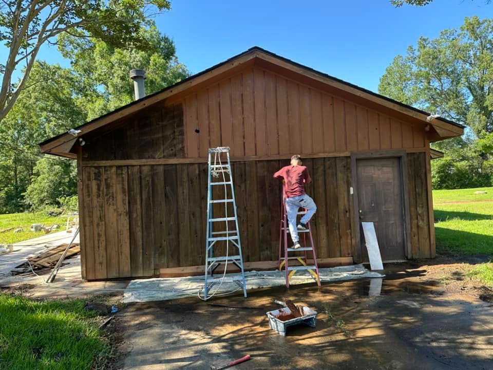 A man is standing on a ladder painting a wooden building.