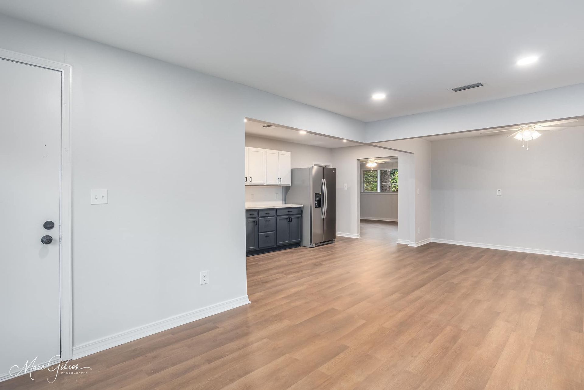 An empty living room with hardwood floors and a refrigerator.