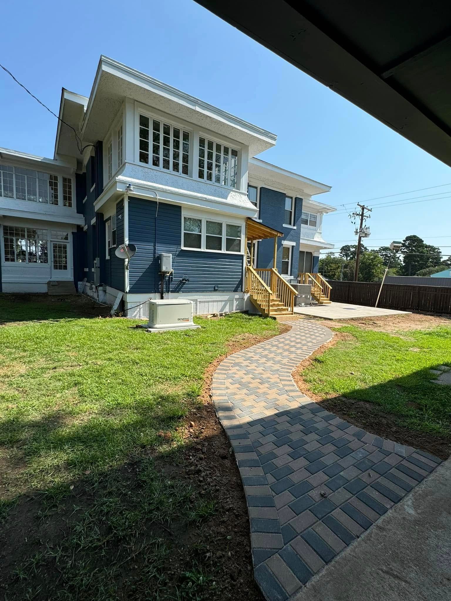 A large blue and white house with a brick walkway leading to it.