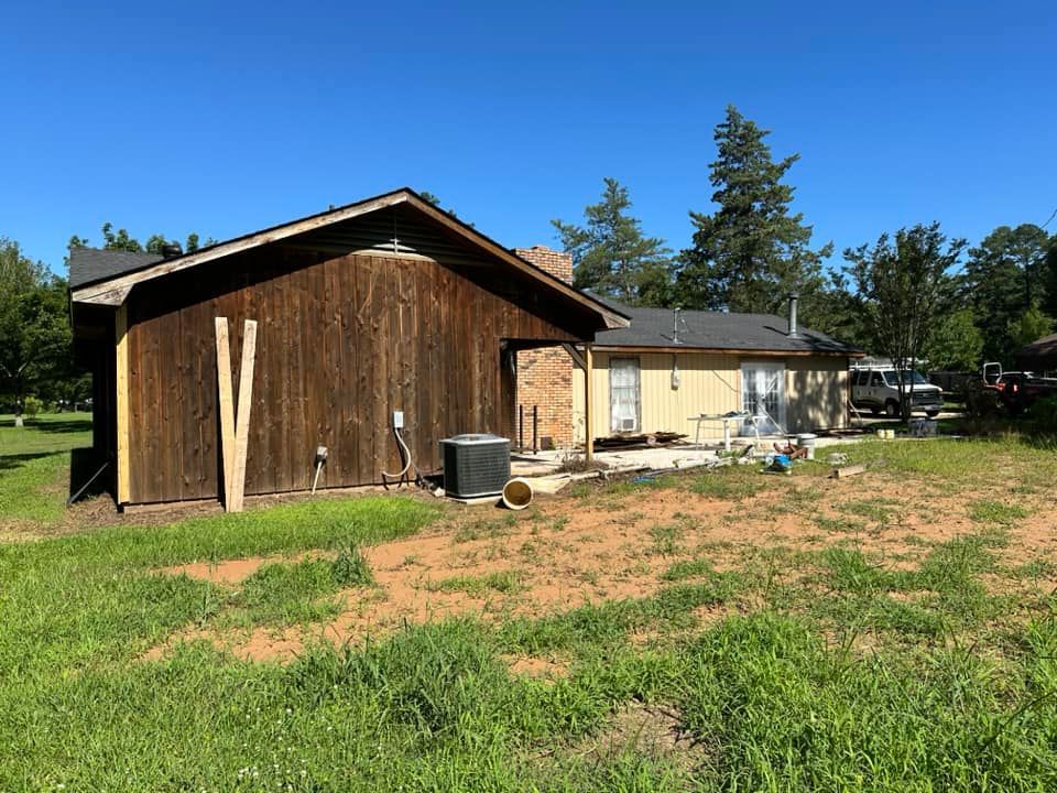 A wooden shed is sitting in the middle of a grassy field next to a house.