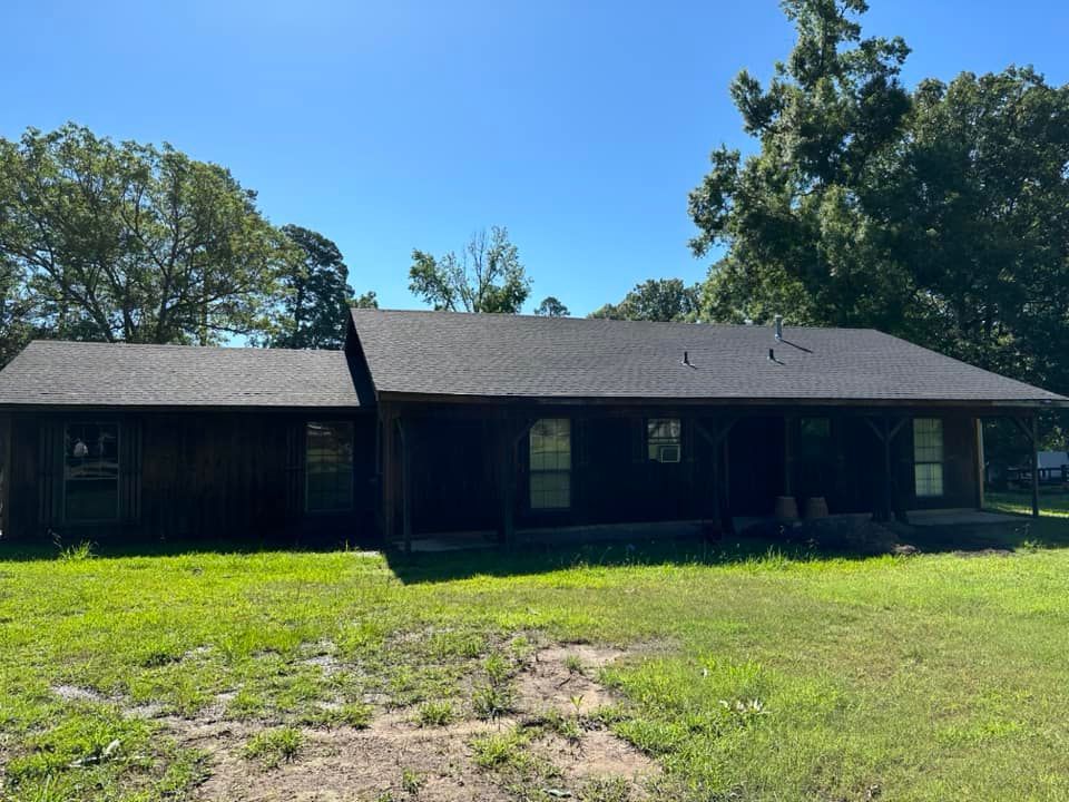 A house with a black roof is sitting on top of a lush green field.