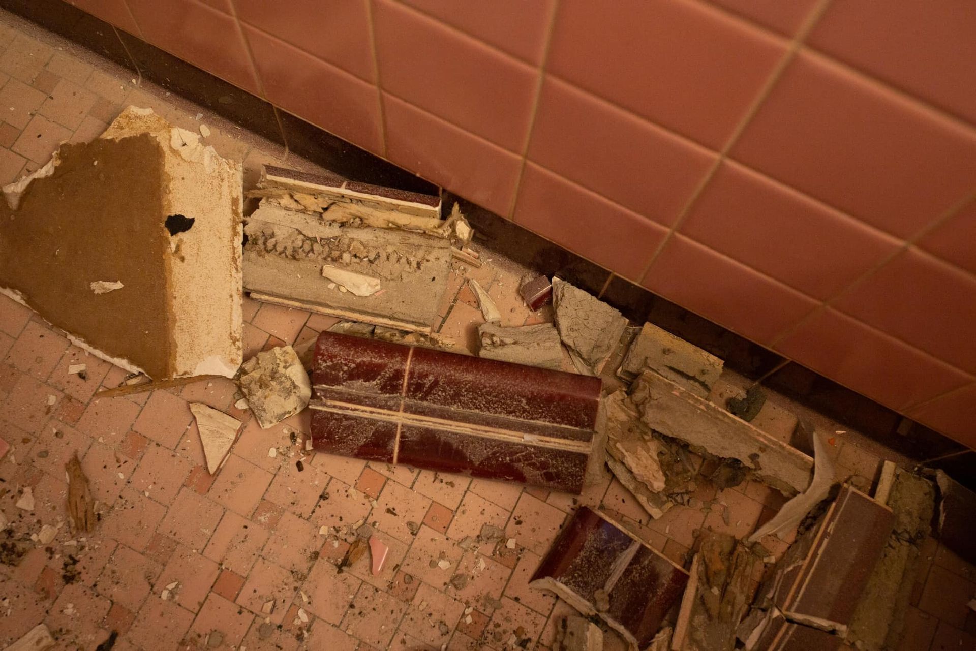 A broken tile is laying on the floor next to a wall.