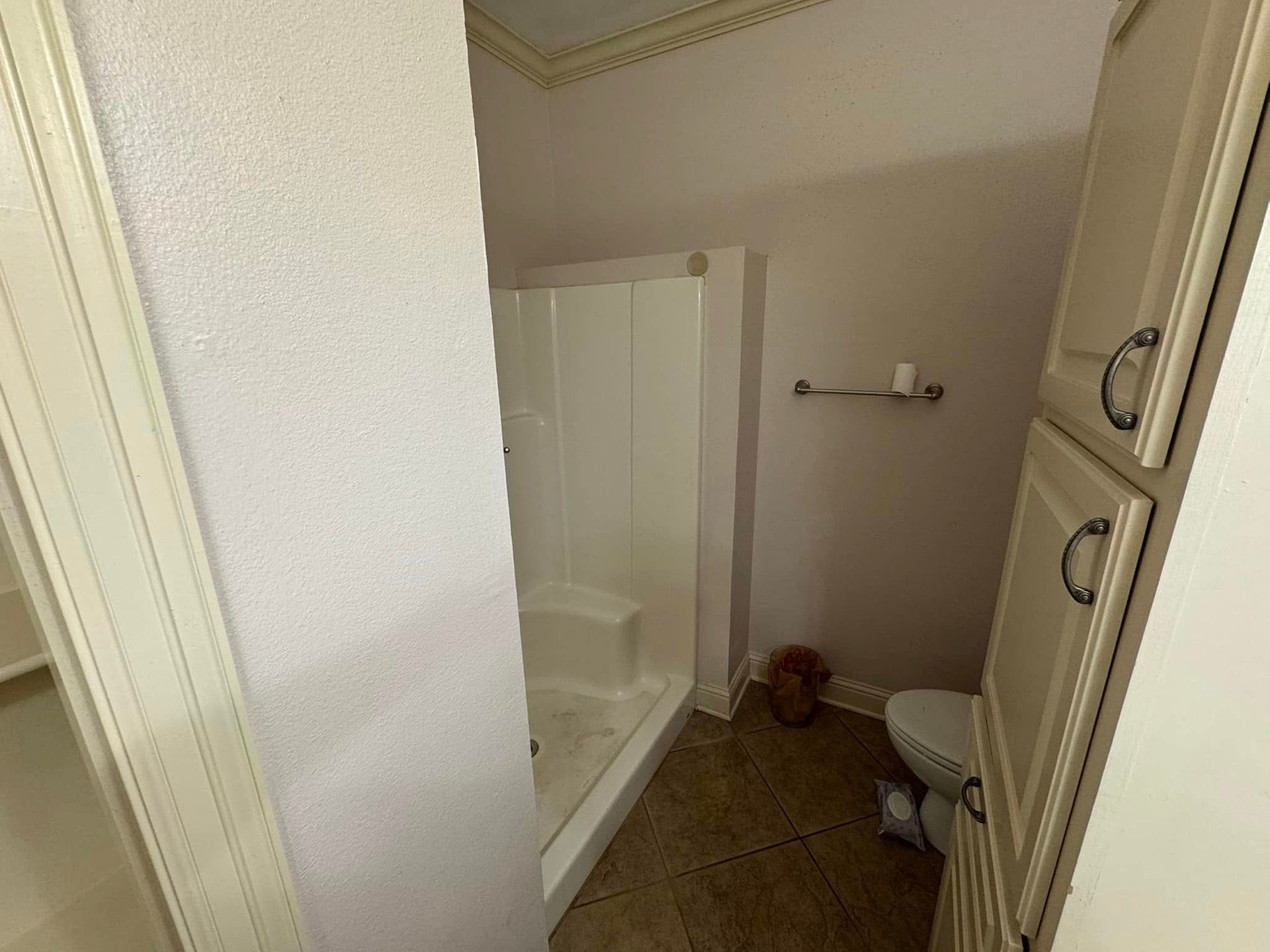 A bathroom with a toilet , shower , and cabinets.