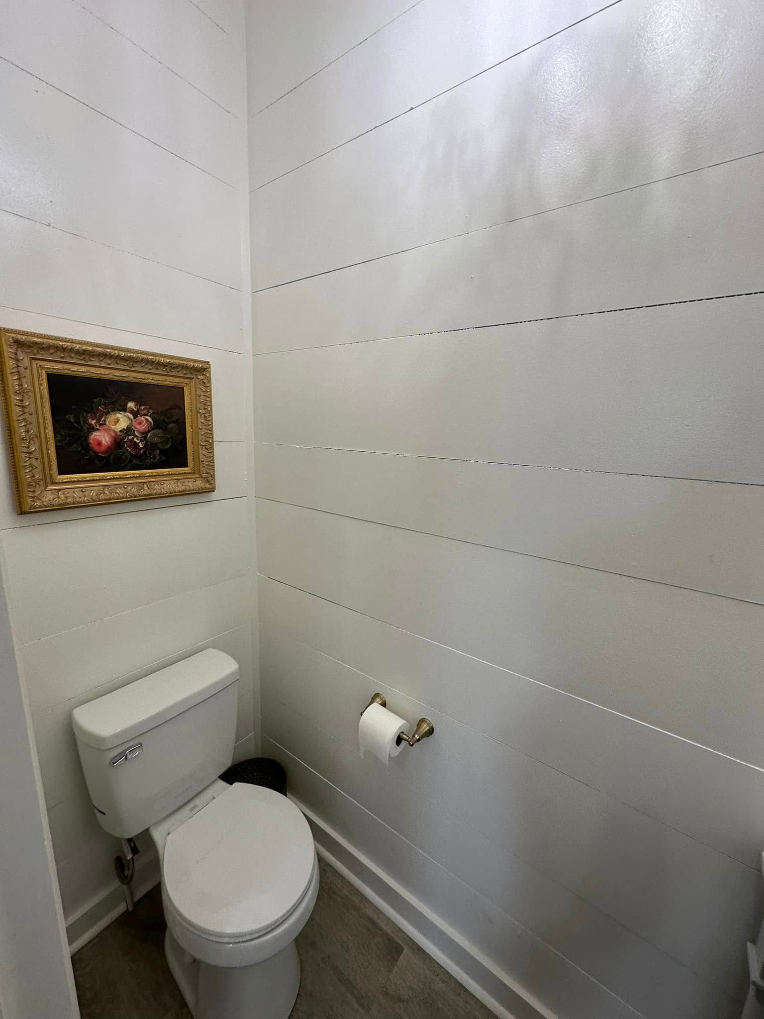 A toilet in a bathroom with a picture on the wall above it.