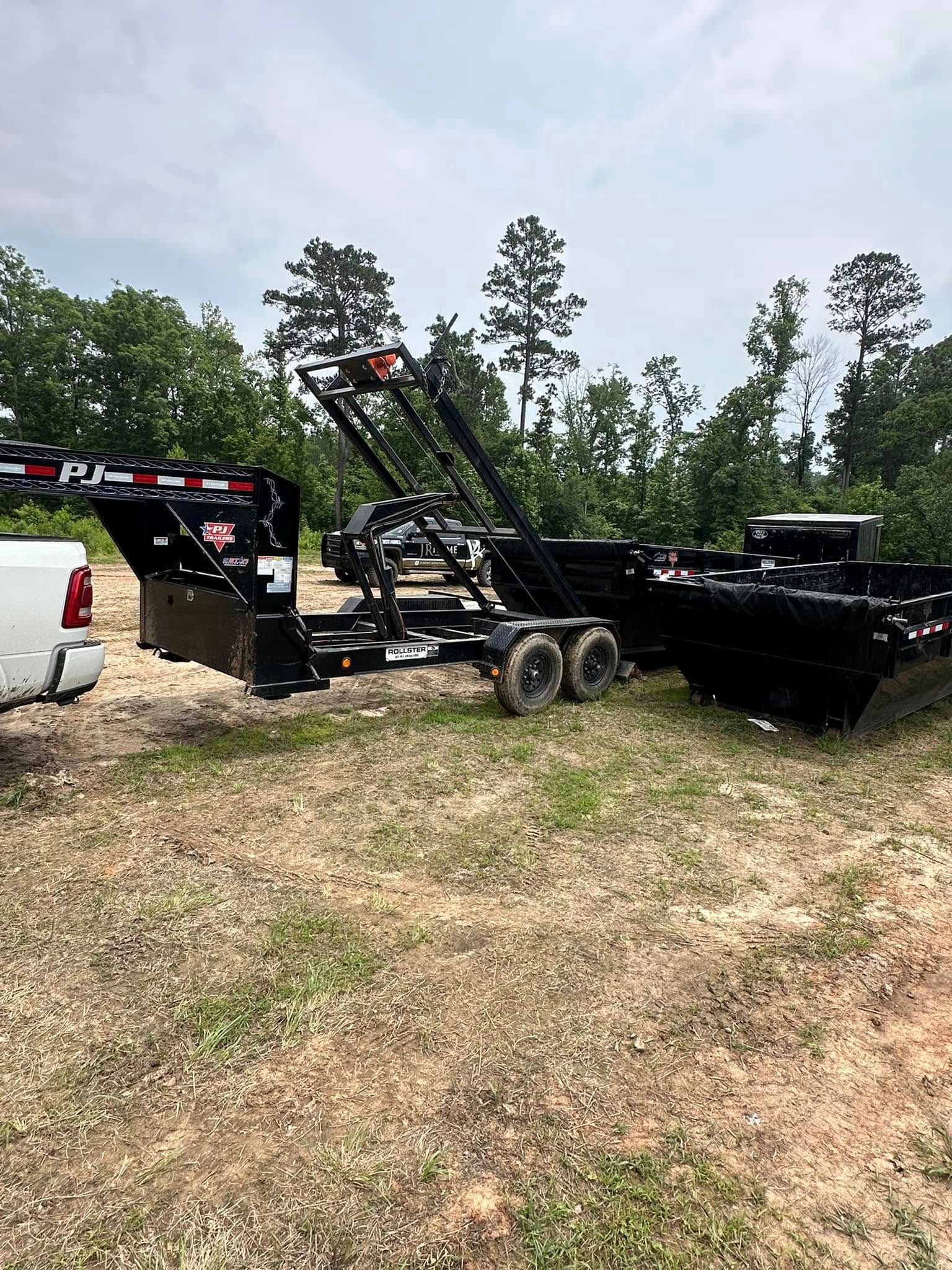 A dump trailer is parked in a grassy field next to a truck.