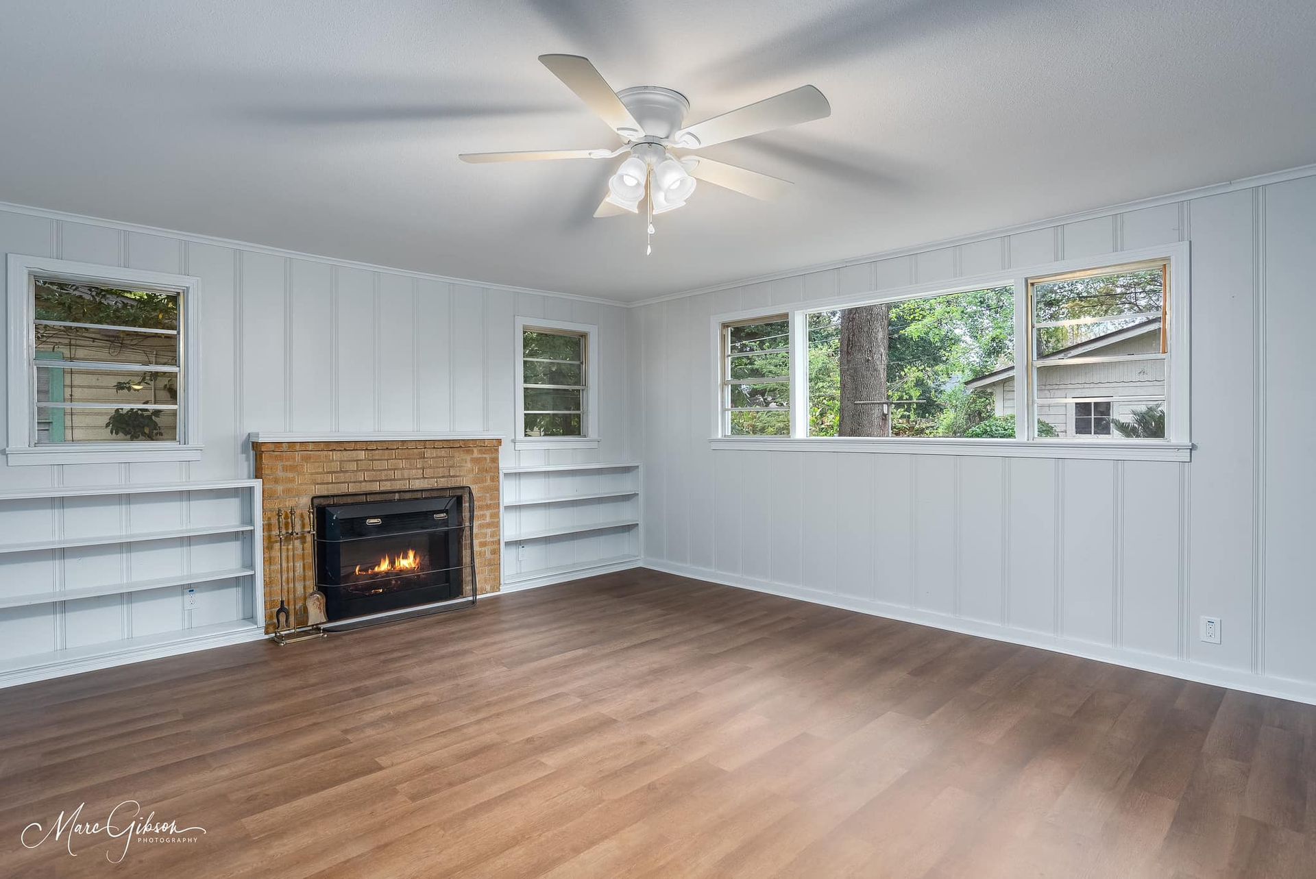 An empty living room with a fireplace and ceiling fan.