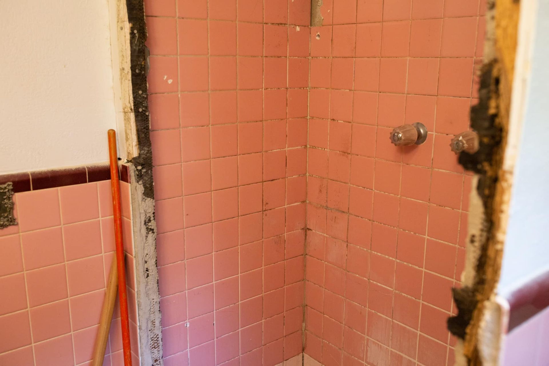 A bathroom with pink tiles and a broom.