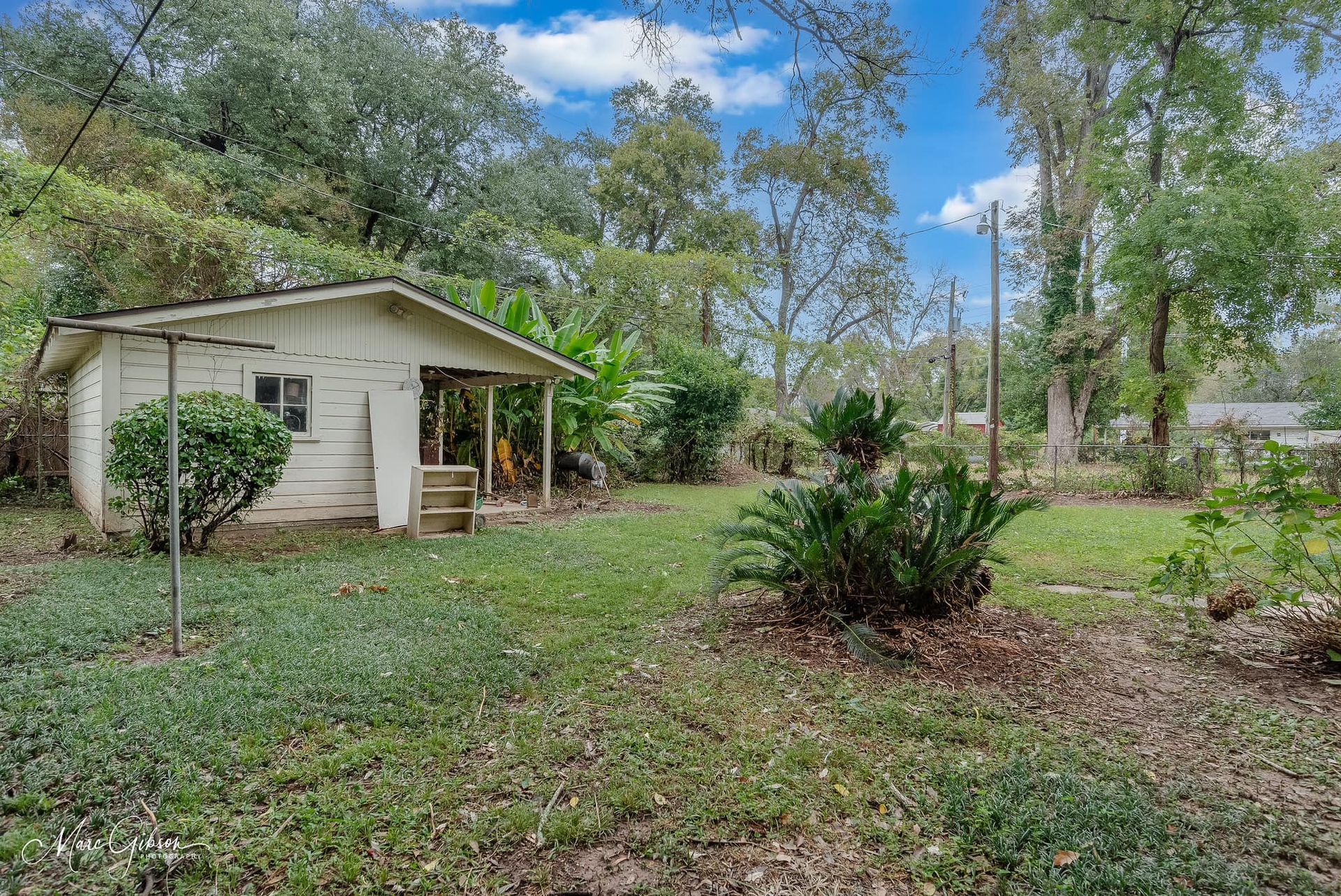 A small white house is sitting in the middle of a grassy yard surrounded by trees.
