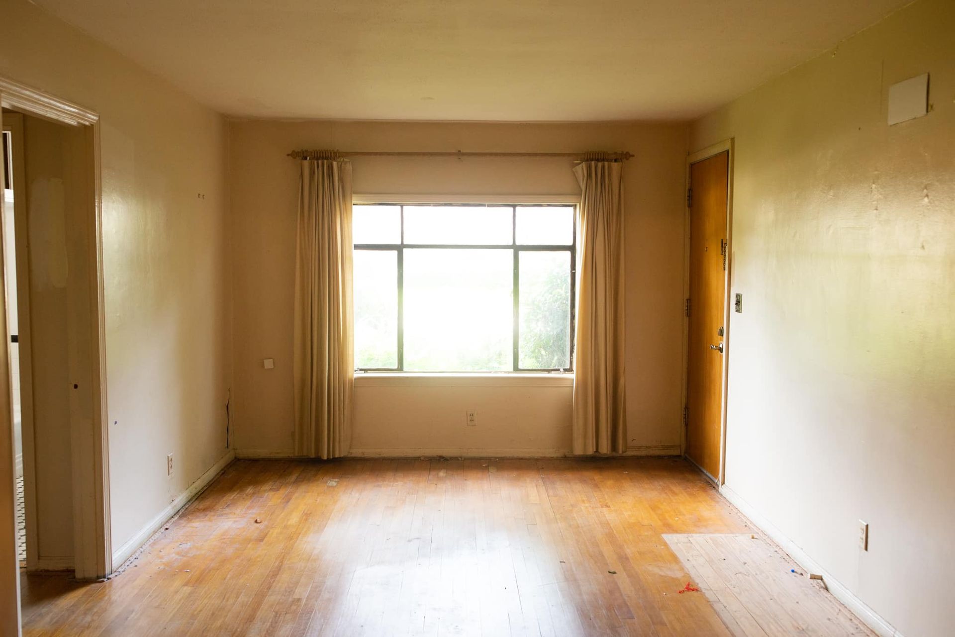 An empty living room with hardwood floors and a large window.
