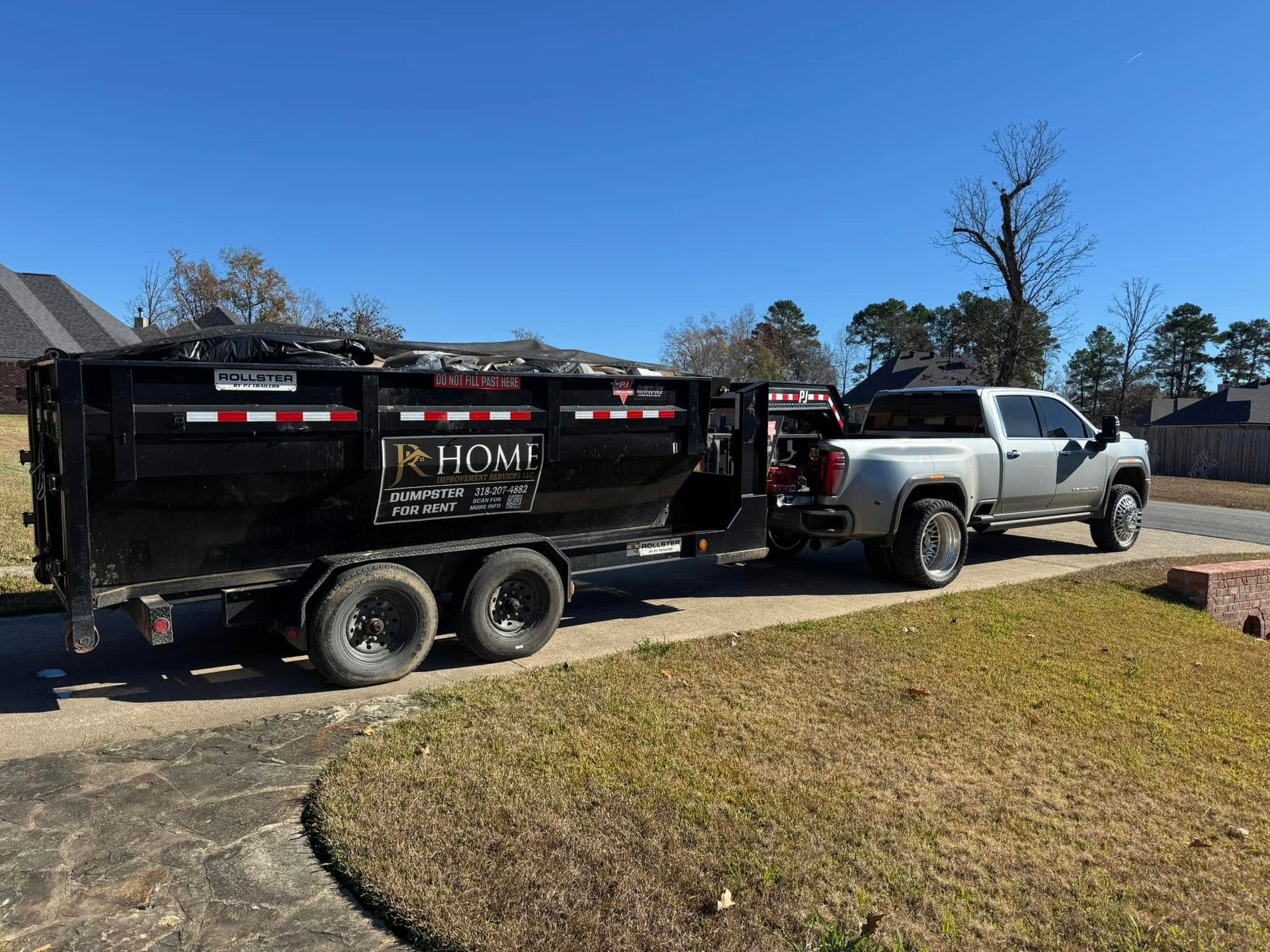 A dumpster is being towed by a truck in a driveway.