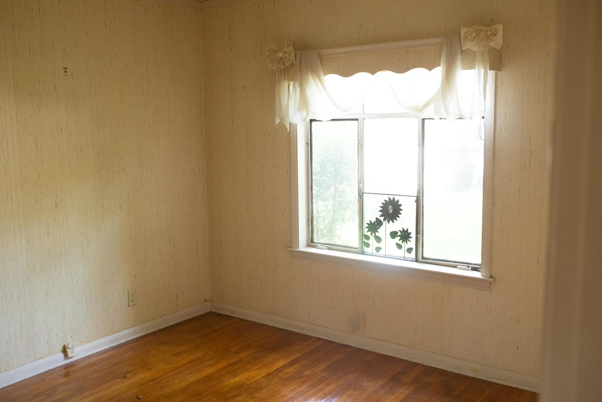 An empty room with a window and a wooden floor.
