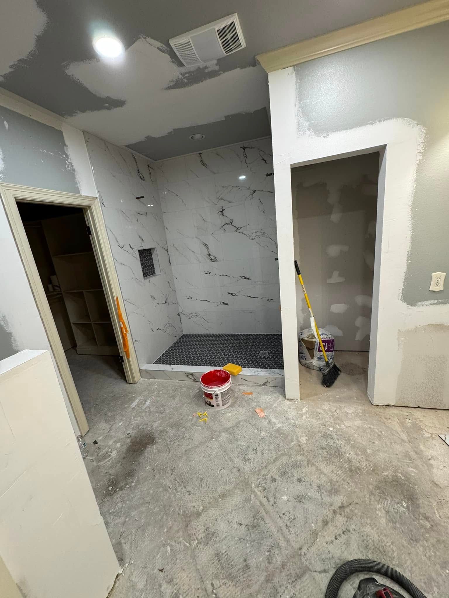 A bathroom under construction with a walk in shower and a bucket of paint on the floor.