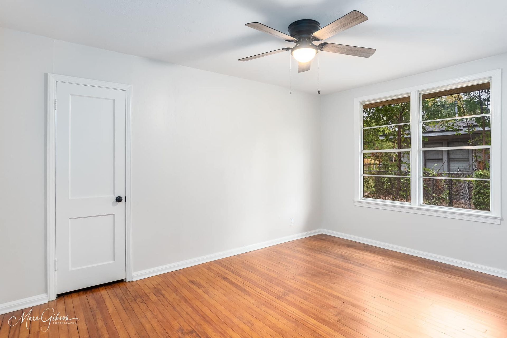 An empty room with hardwood floors and a ceiling fan.