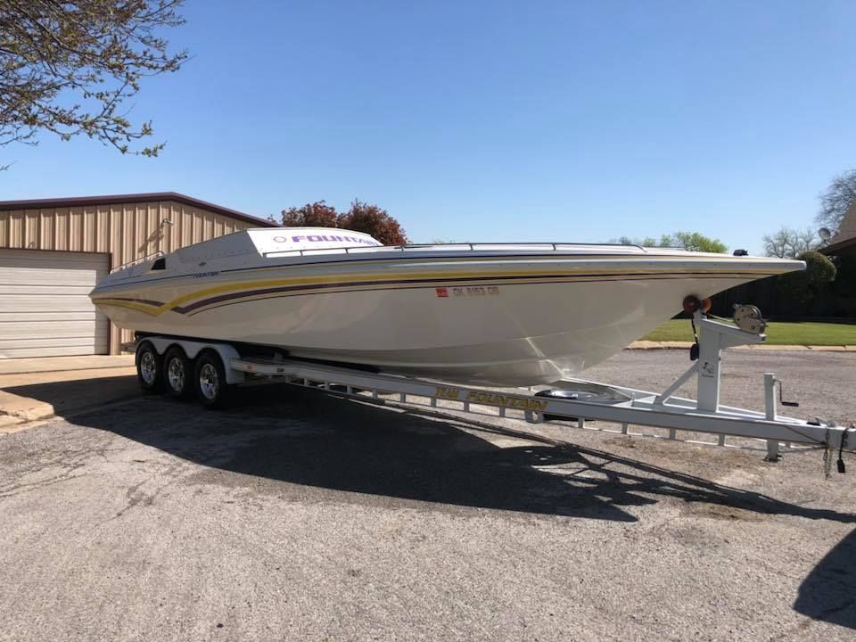 White speedboat on a triple-axle trailer in a parking lot under a clear blue sky