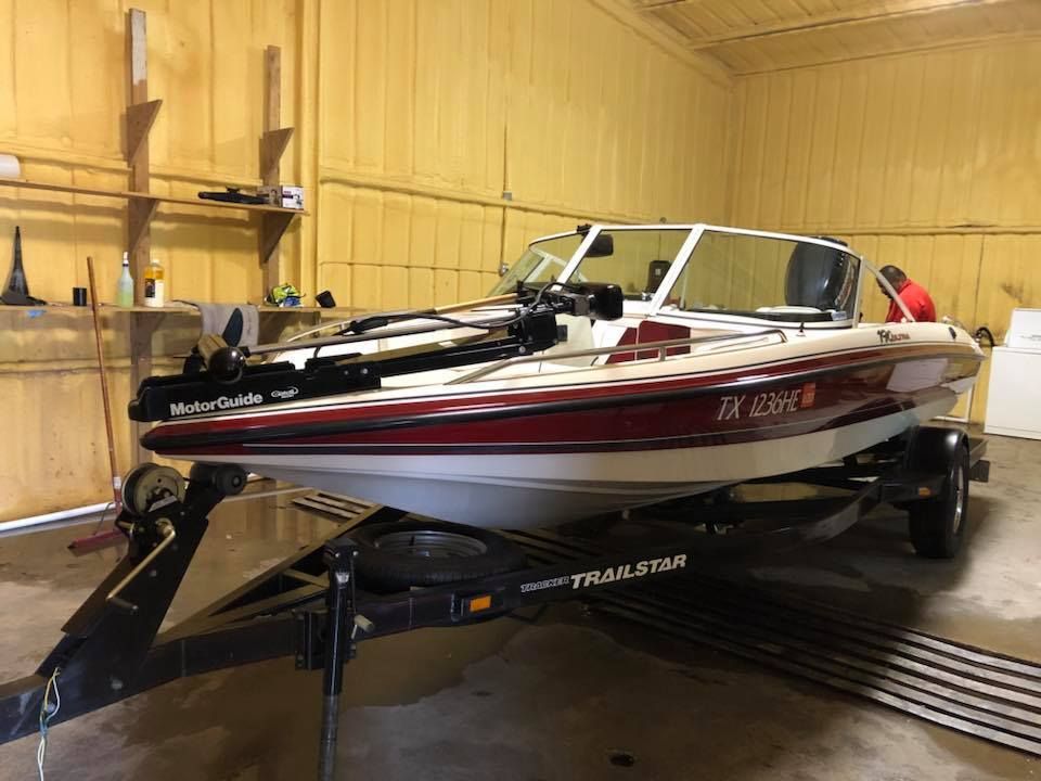 Red and white motorboat on a trailer inside a yellow-walled garage with the hatch open