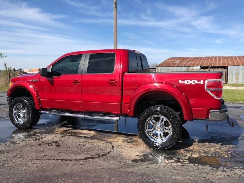 Red lifted pickup truck with chrome wheels parked on wet pavement under a blue sky