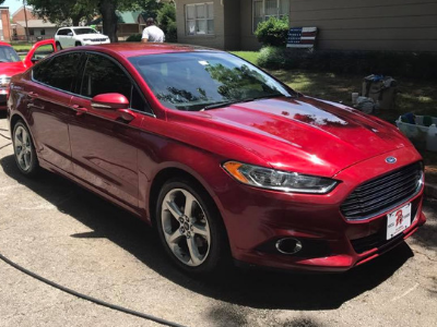 Red sedan parked on a sunlit residential street beside a house