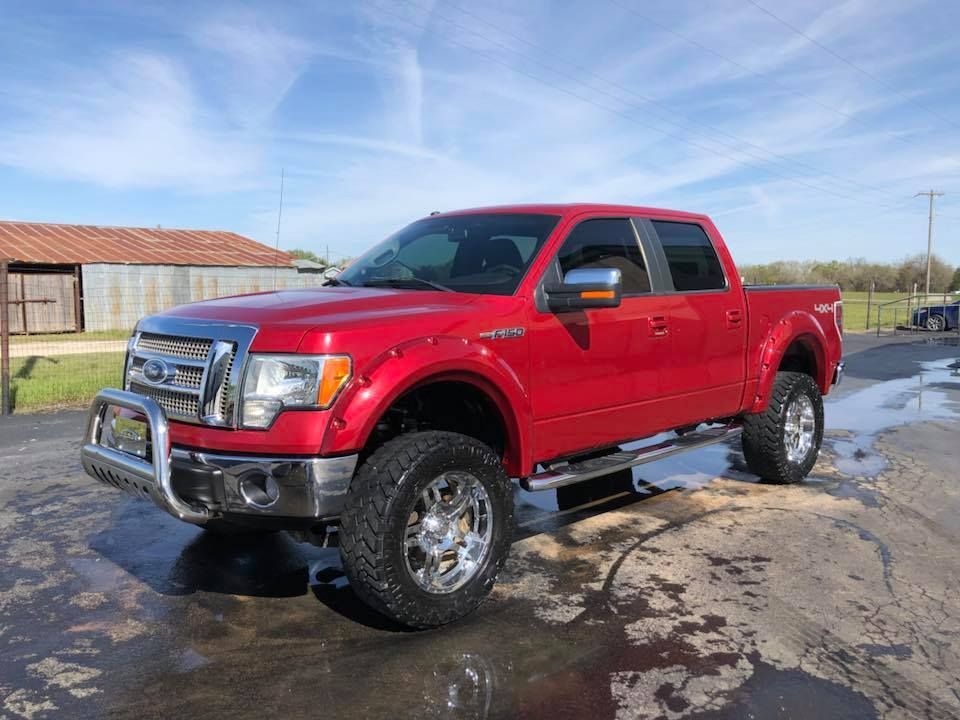 Red lifted pickup truck parked on a wet lot under a blue sky.