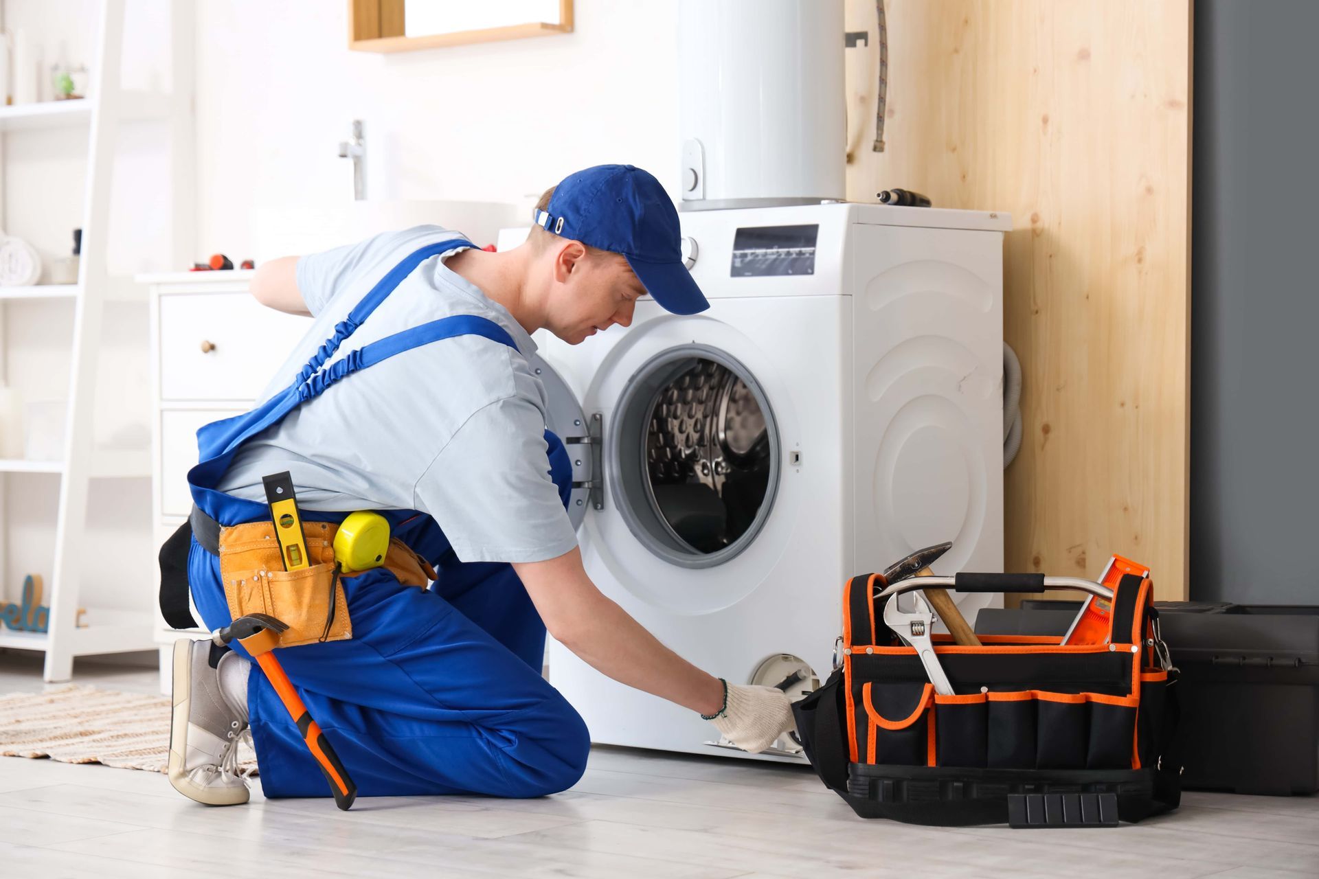 Technician kneeling by a front-loading washing machine, using tools beside an open tool bag.