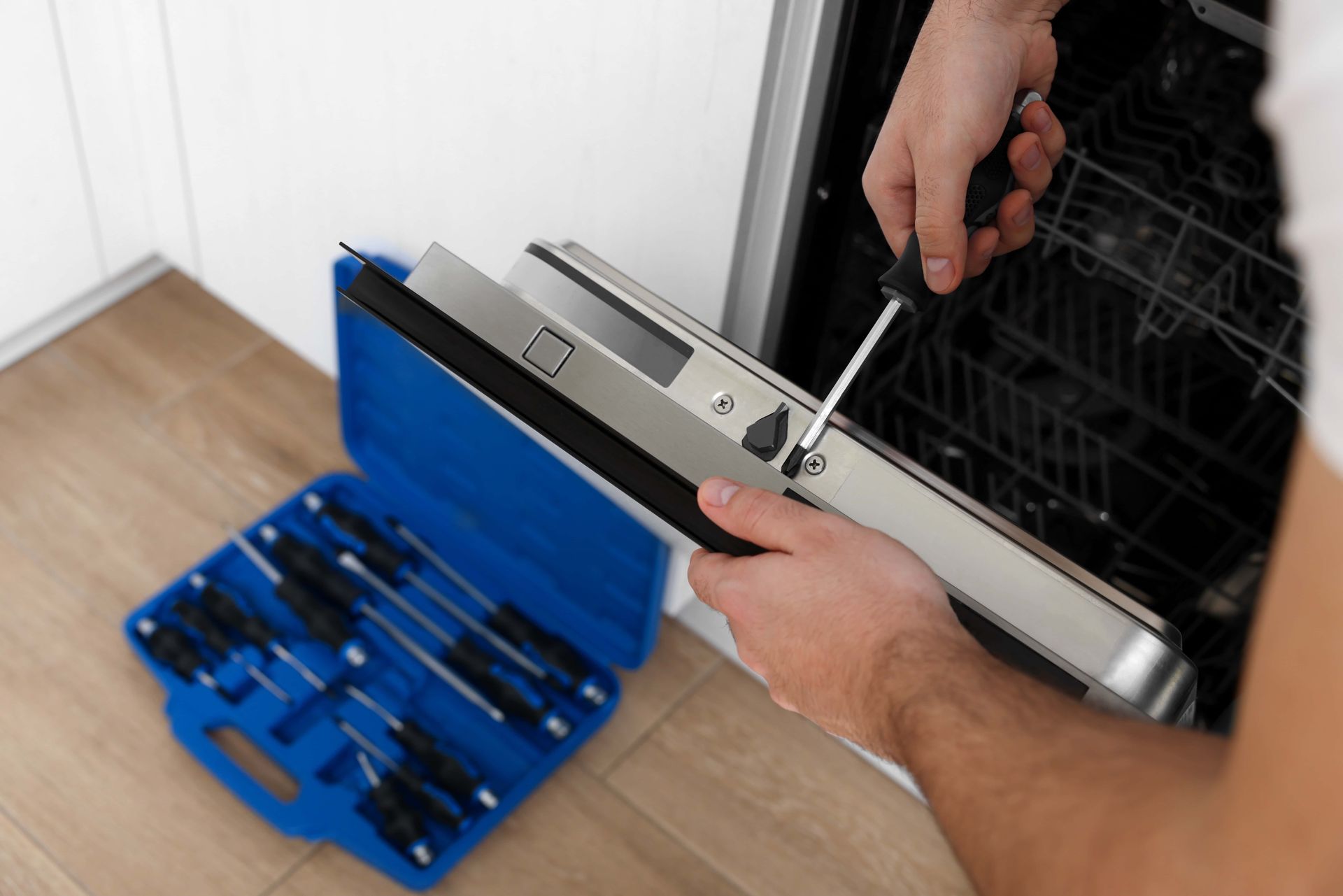 Hands using a screwdriver to repair a black appliance beside a blue tool kit.