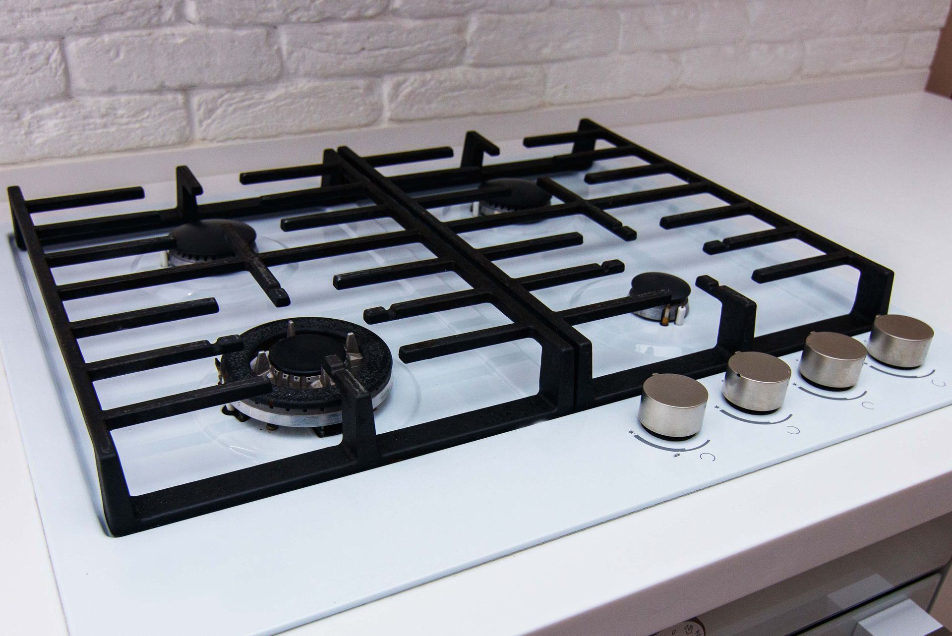 Black gas stovetop with four burners and silver control knobs on a white countertop against a tiled wall