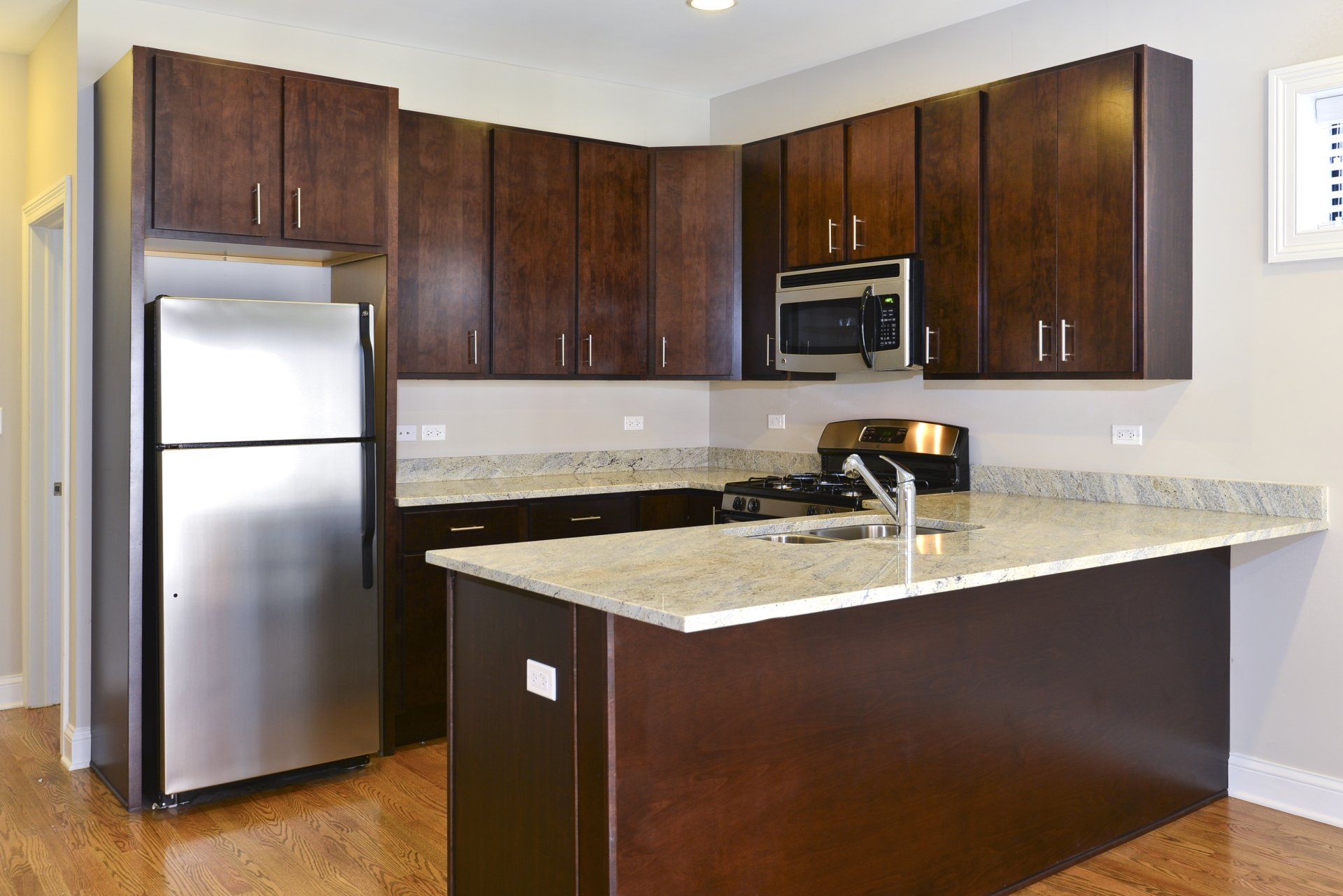 A kitchen with stainless steel appliances, oversized breakfast bar, and wooden cabinets at The Belmont by Reside Flats.