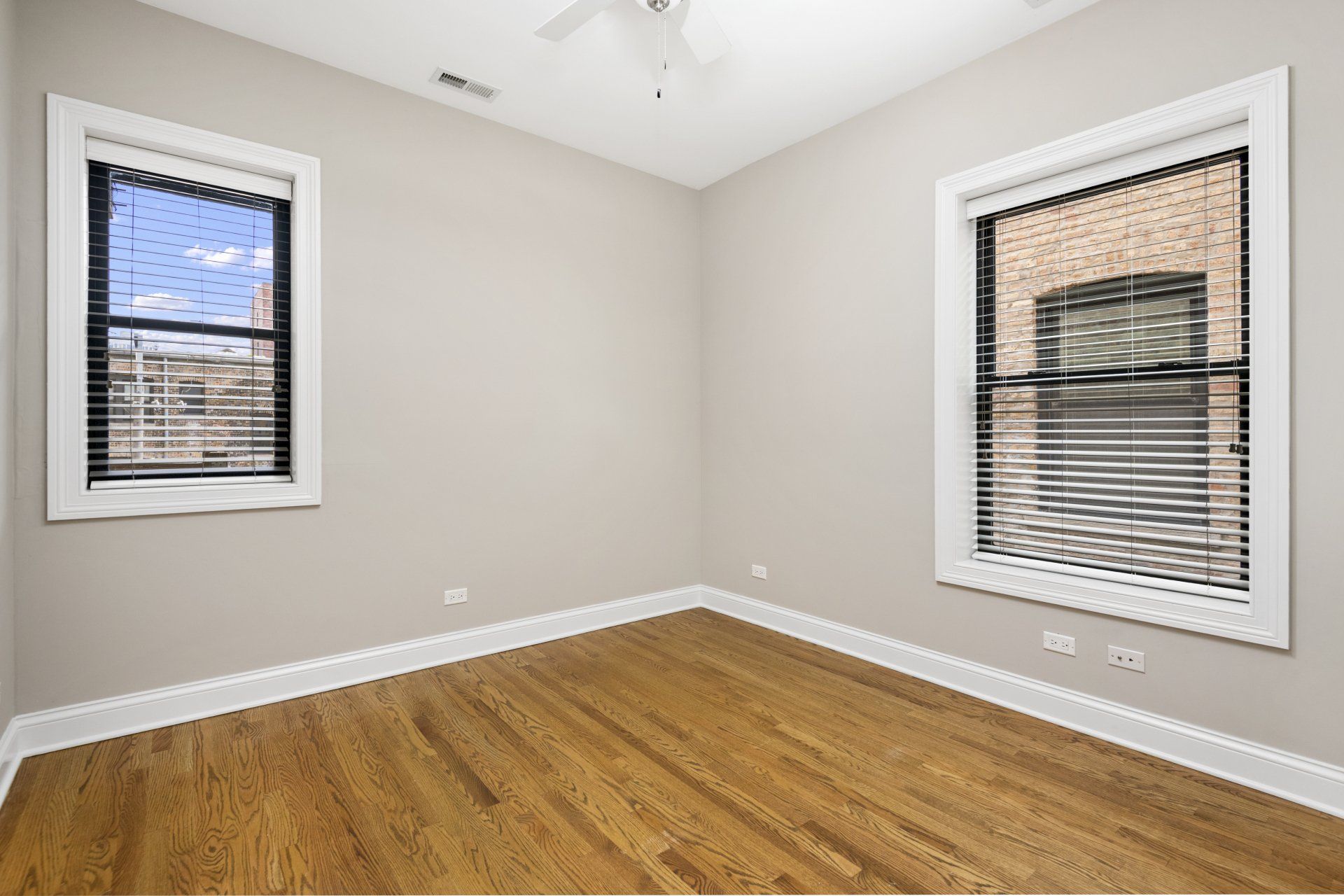 An empty apartment bedroom with hardwood floors and two windows.