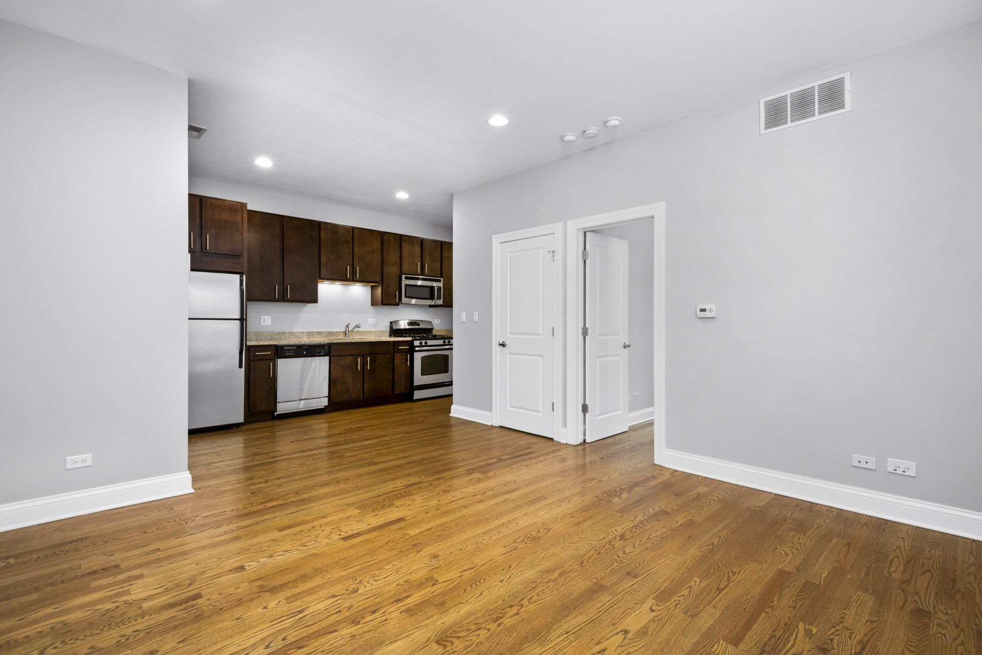 An empty open floor plan apartment with hardwood floors and a kitchen.