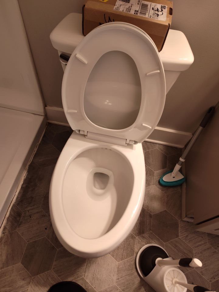 A toilet with the lid open in a bathroom next to a box.
