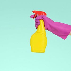 A person wearing a purple glove is holding a yellow spray bottle.