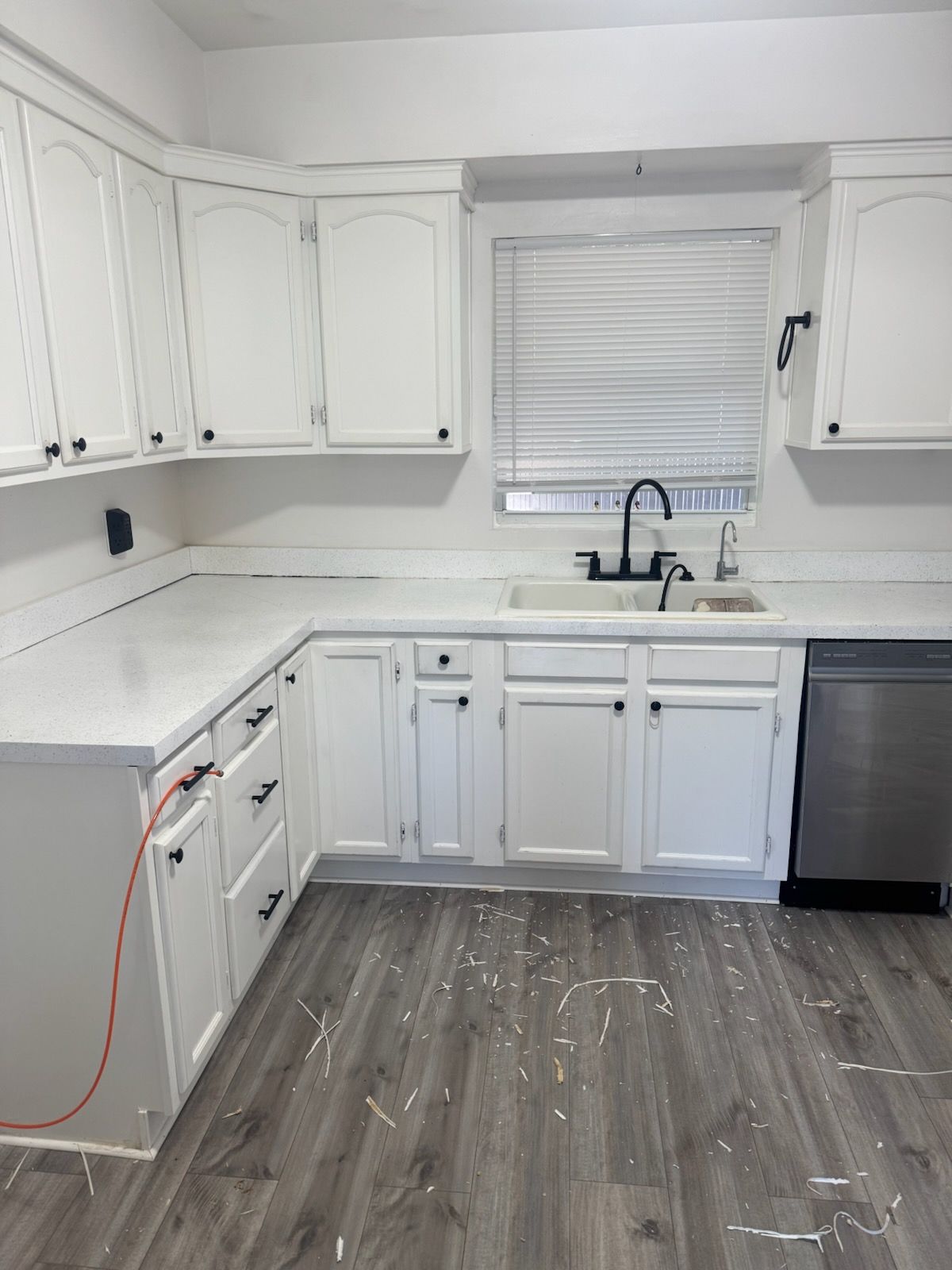 White kitchen with cabinets, sink under window, gray floor, and stainless dishwasher.