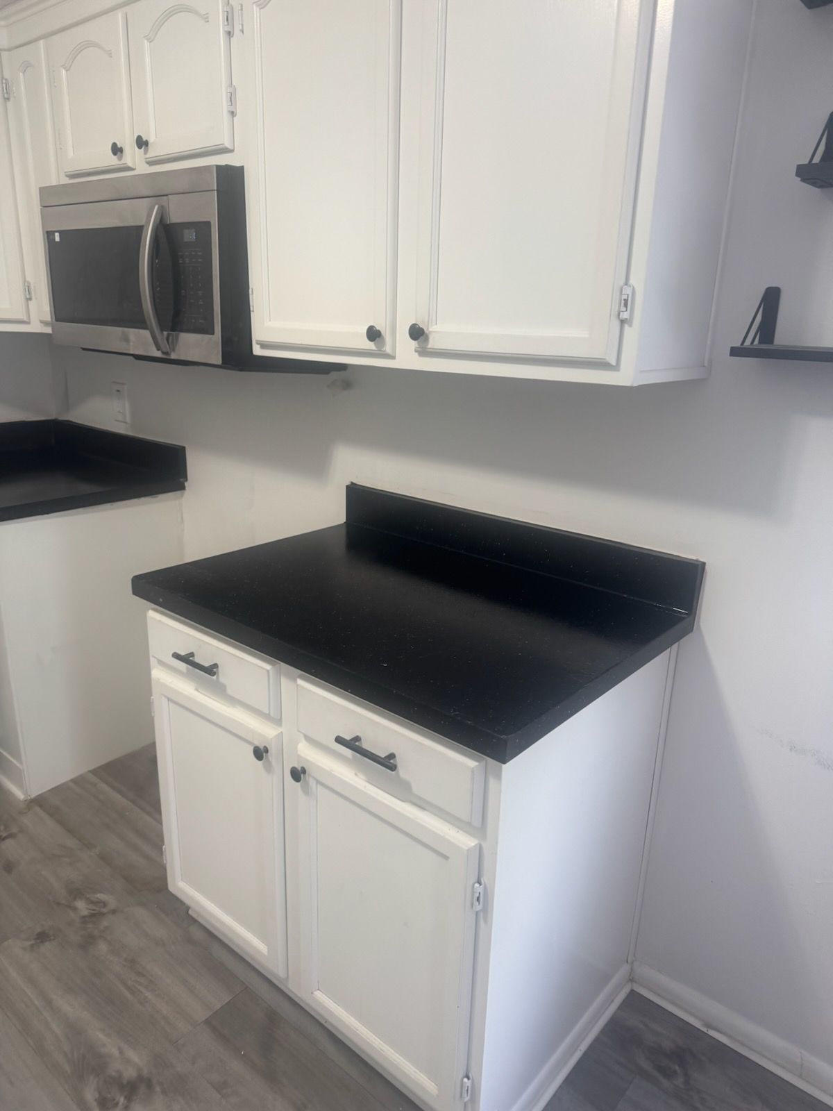 Small kitchen with white cabinets, black countertops, and a stainless steel microwave.