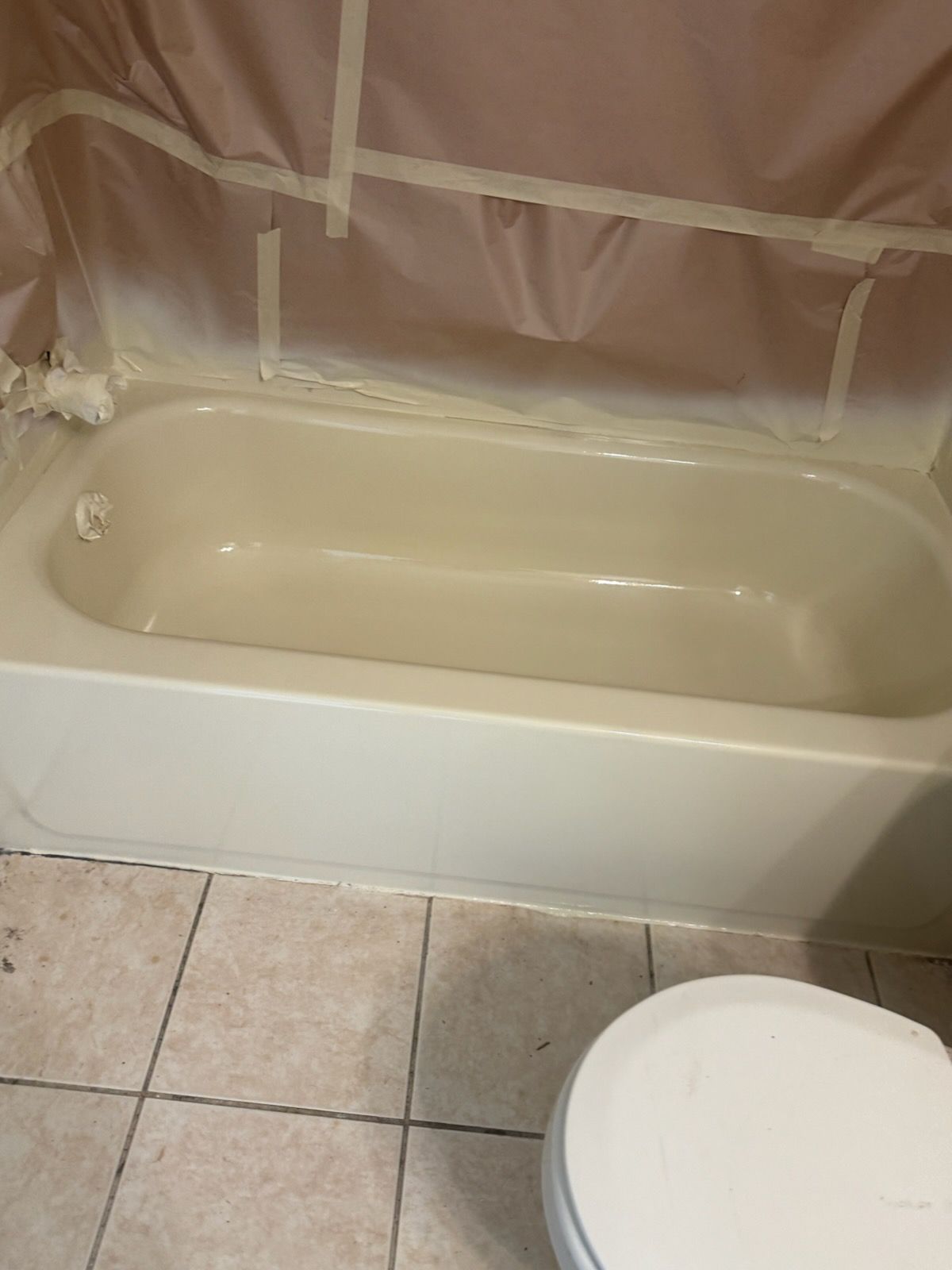 Bathtub with beige tile floor and a partially covered wall behind it.