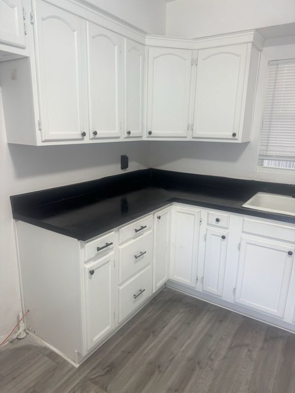 White kitchen with black countertops, white cabinets, and gray wood-look flooring.